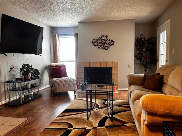 living room featuring baseboards, a textured ceiling, wood finished floors, and a tiled fireplace