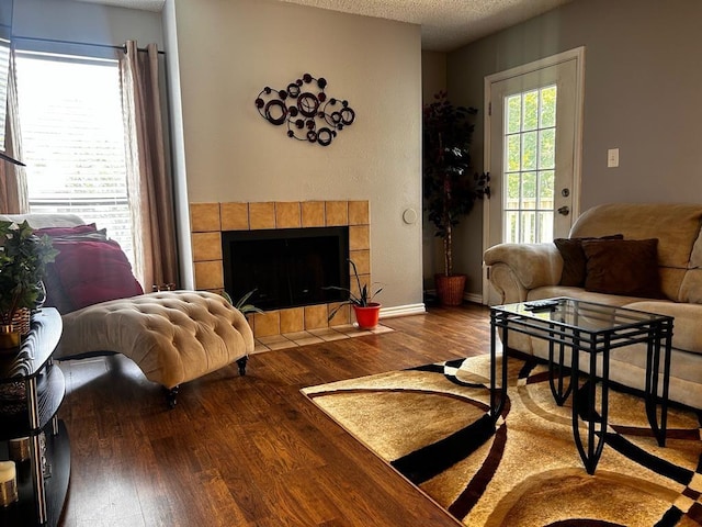 living area with a tile fireplace, a textured ceiling, baseboards, and wood finished floors