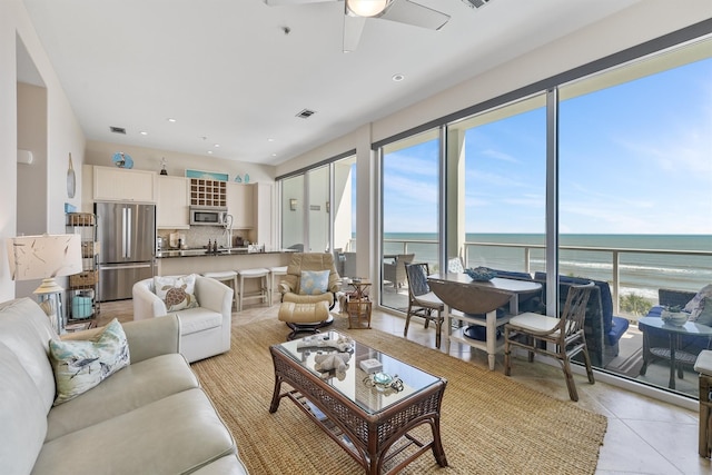 living room with light tile patterned flooring, visible vents, a water view, and a ceiling fan