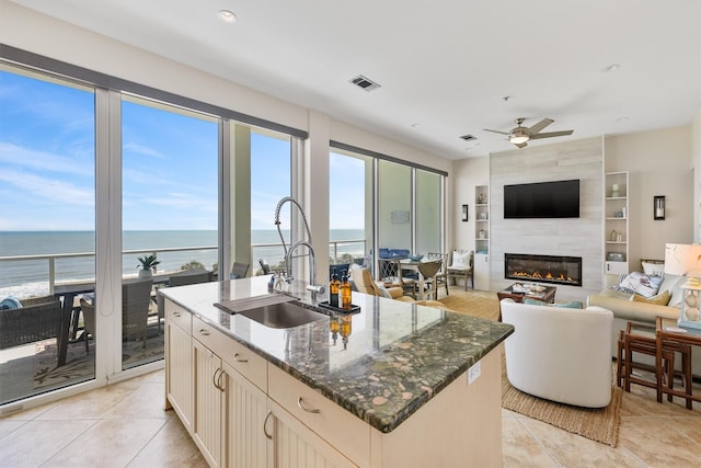 kitchen featuring a sink, a large fireplace, a kitchen island with sink, visible vents, and ceiling fan