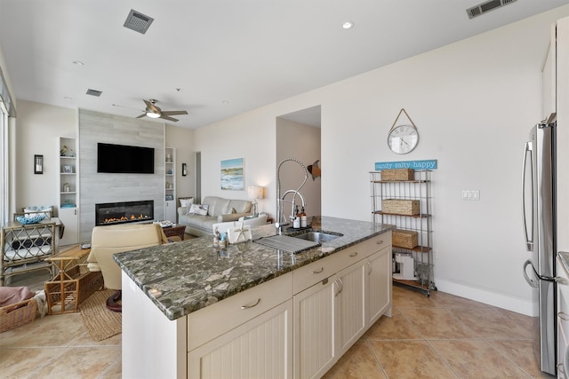 kitchen with open floor plan, dark stone countertops, a sink, visible vents, and a ceiling fan