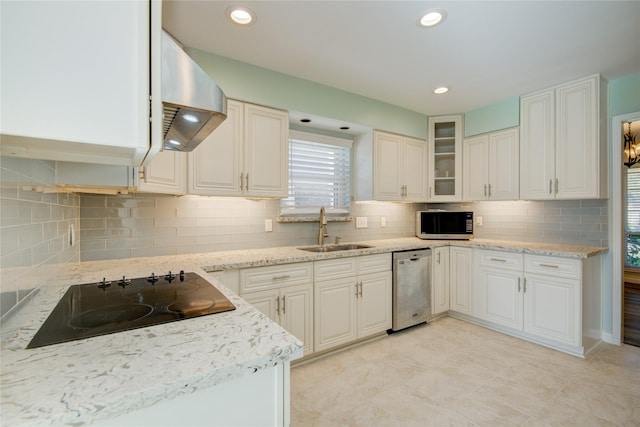 kitchen with stainless steel appliances, backsplash, wall chimney range hood, a sink, and light stone countertops