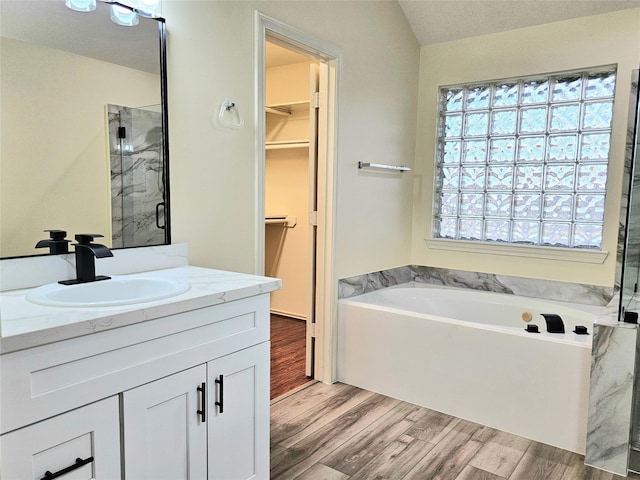 bathroom with a stall shower, a spacious closet, wood finished floors, a garden tub, and vanity