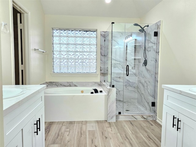 bathroom featuring a bath, wood finished floors, vanity, and a marble finish shower