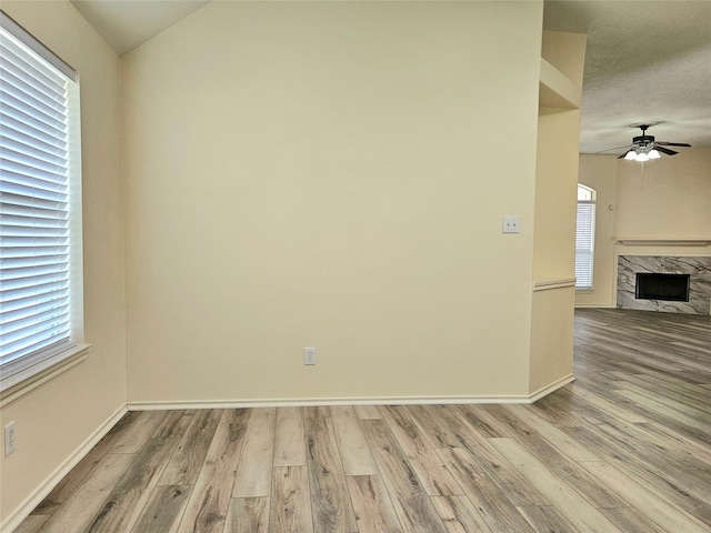 unfurnished room with baseboards, wood finished floors, a fireplace, and ceiling fan