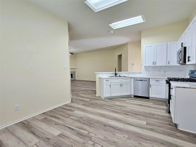 kitchen featuring a peninsula, light wood-style flooring, appliances with stainless steel finishes, and a sink
