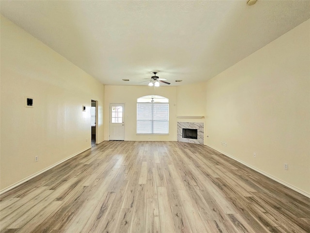 unfurnished living room with ceiling fan, baseboards, a high end fireplace, and light wood-style flooring