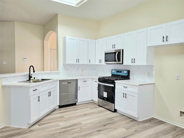 kitchen with a peninsula, a sink, light wood-type flooring, backsplash, and appliances with stainless steel finishes