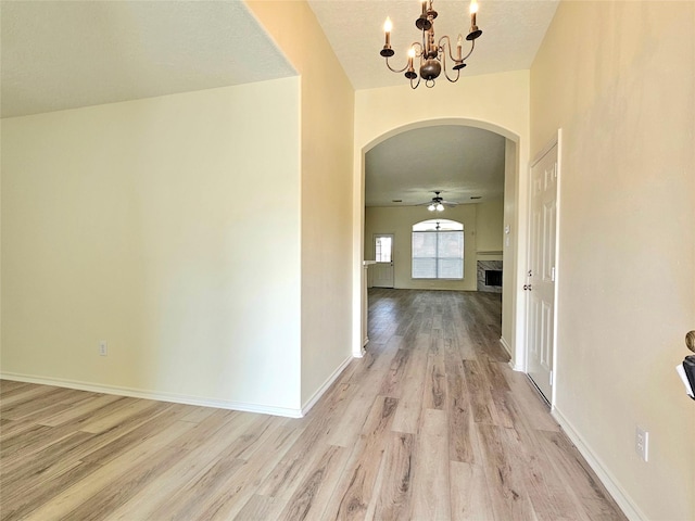 hallway featuring arched walkways, light wood-style flooring, baseboards, and a notable chandelier