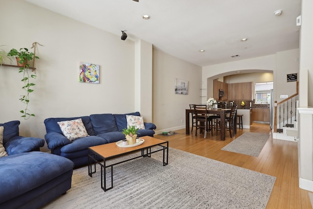 living area featuring arched walkways, stairs, light wood-style floors, recessed lighting, and baseboards