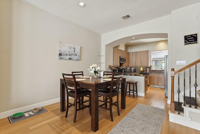 dining room featuring arched walkways, light wood-style flooring, stairway, recessed lighting, and baseboards