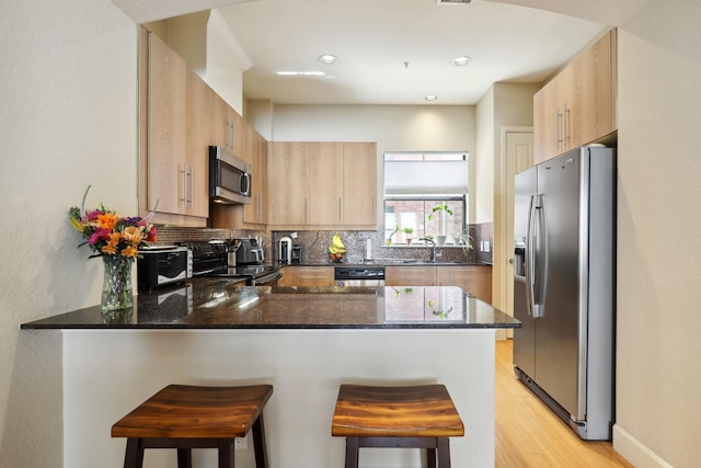 kitchen with stainless steel appliances, light brown cabinetry, a peninsula, a sink, and backsplash