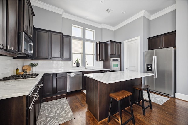 kitchen featuring a kitchen bar, stainless steel appliances, a center island, a sink, and dark wood-style floors