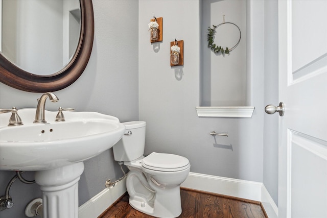 half bath with baseboards, toilet, a sink, and wood finished floors