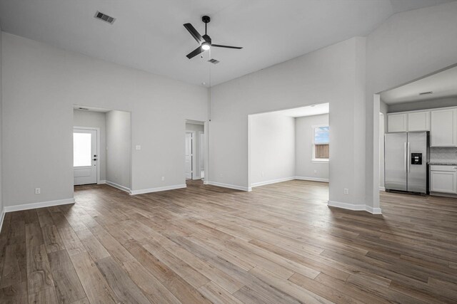 unfurnished living room with visible vents, a ceiling fan, a high ceiling, and wood finished floors