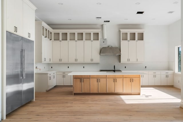 kitchen with light wood-type flooring, glass insert cabinets, a kitchen island, stainless steel built in fridge, and a sink