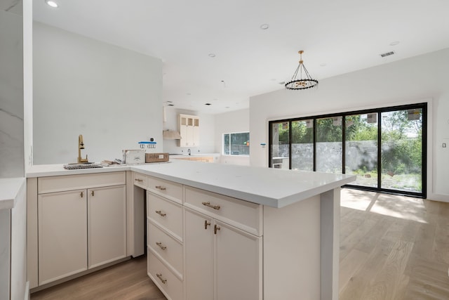 kitchen with a peninsula, light countertops, visible vents, light wood finished floors, and a sink