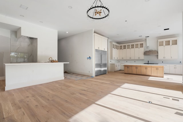 kitchen featuring light wood-style flooring, wall chimney range hood, a center island, built in fridge, and baseboards