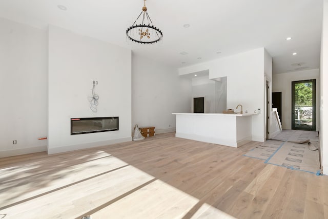 unfurnished living room with light wood-type flooring, baseboards, a glass covered fireplace, and recessed lighting