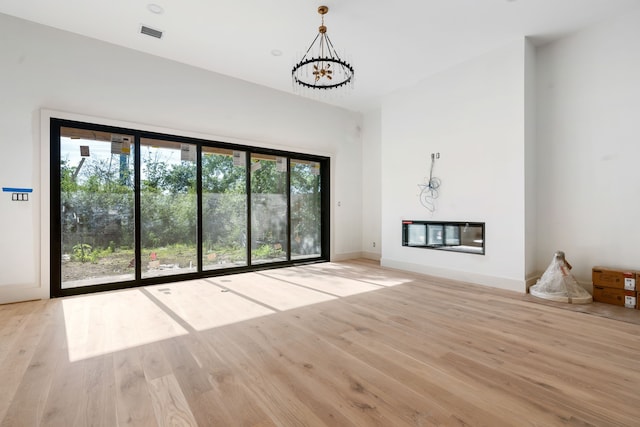 unfurnished living room with a chandelier, a glass covered fireplace, light wood-type flooring, and baseboards
