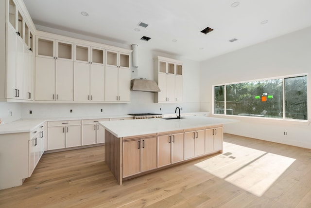 kitchen with light wood-style flooring, a kitchen island with sink, visible vents, wall chimney exhaust hood, and a sink