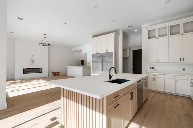 kitchen featuring a glass covered fireplace, light wood-type flooring, a kitchen island with sink, stainless steel appliances, and a sink