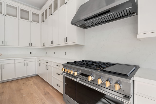 kitchen featuring wall chimney range hood, high end stainless steel range, light wood-style floors, and light countertops