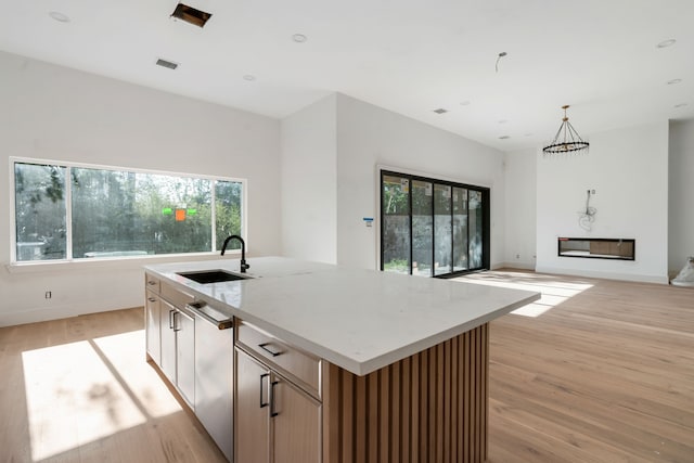 kitchen featuring light wood-style floors, light stone countertops, a sink, a center island with sink, and baseboards