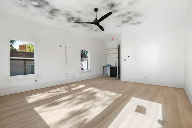 unfurnished living room featuring a sink, light wood-style flooring, a ceiling fan, and baseboards