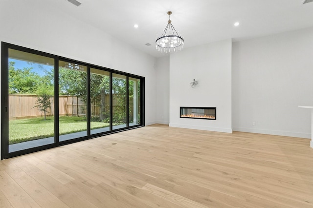 6536 Community Dr, West University Place, TX 77005 - unfurnished living room with light wood-style floors, a glass covered fireplace, recessed lighting, a chandelier, and a towering ceiling