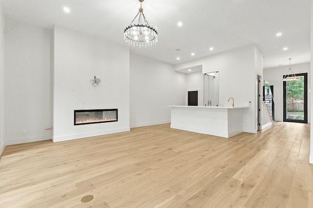 6536 Community Dr, West University Place, TX 77005 - unfurnished living room with light wood-style floors, a chandelier, recessed lighting, and a glass covered fireplace