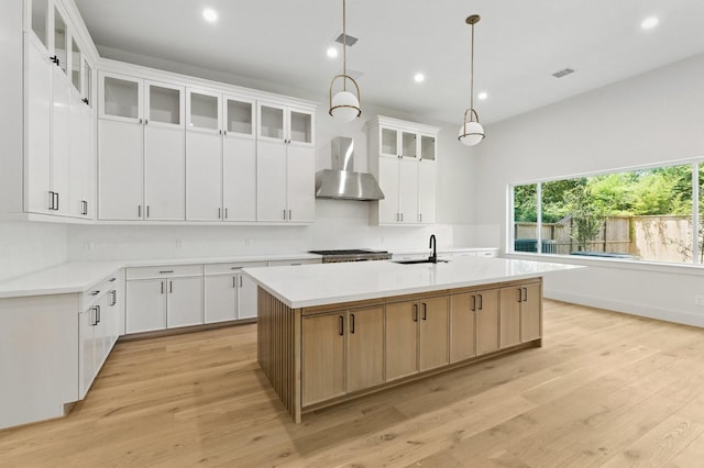 6536 Community Dr, West University Place, TX 77005 - kitchen with wall chimney range hood, an island with sink, recessed lighting, light wood finished floors, and light countertops