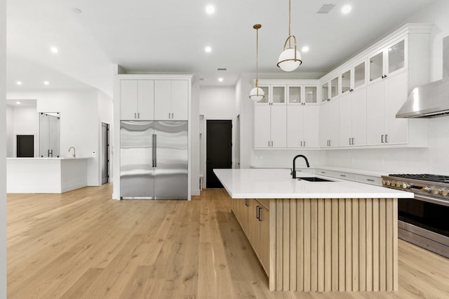 6536 Community Dr, West University Place, TX 77005 - kitchen with appliances with stainless steel finishes, wall chimney exhaust hood, a kitchen island with sink, light countertops, and light wood-style flooring