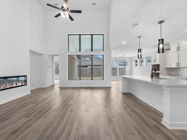 3193 Stingray Cove Dr, Katy, TX 77493 - unfurnished living room with a ceiling fan, wood finished floors, a glass covered fireplace, and a high ceiling
