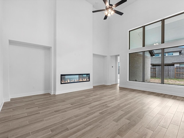 3193 Stingray Cove Dr, Katy, TX 77493 - unfurnished living room featuring a towering ceiling, wood finished floors, ceiling fan, and a glass covered fireplace