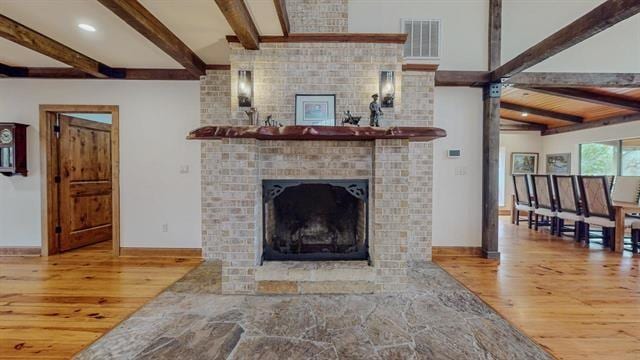 living area with beamed ceiling, a fireplace, visible vents, and wood finished floors