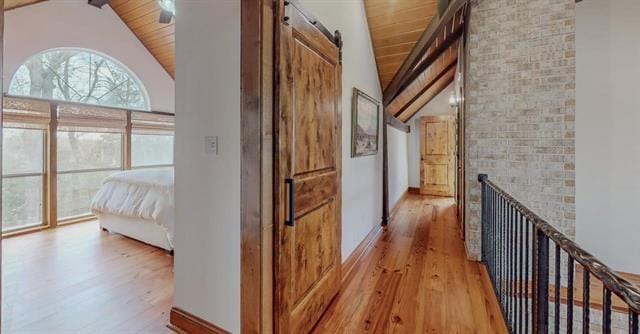 corridor featuring a barn door, vaulted ceiling with beams, wood ceiling, and light wood finished floors
