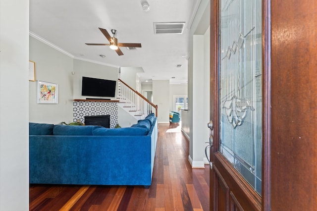 living room with visible vents, crown molding, a fireplace, ceiling fan, and dark wood finished floors