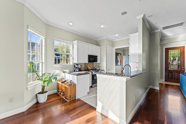 kitchen featuring a peninsula, white cabinets, black microwave, and stainless steel gas range