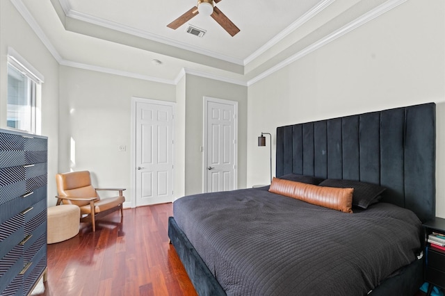 bedroom featuring visible vents, a tray ceiling, crown molding, and wood finished floors