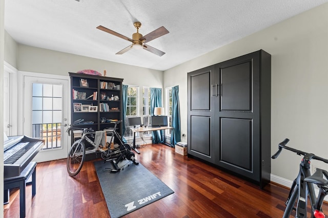 workout area featuring dark wood-style floors, ceiling fan, baseboards, and a textured ceiling
