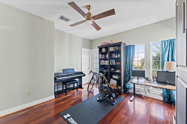workout area featuring a ceiling fan, wood finished floors, a textured ceiling, baseboards, and visible vents