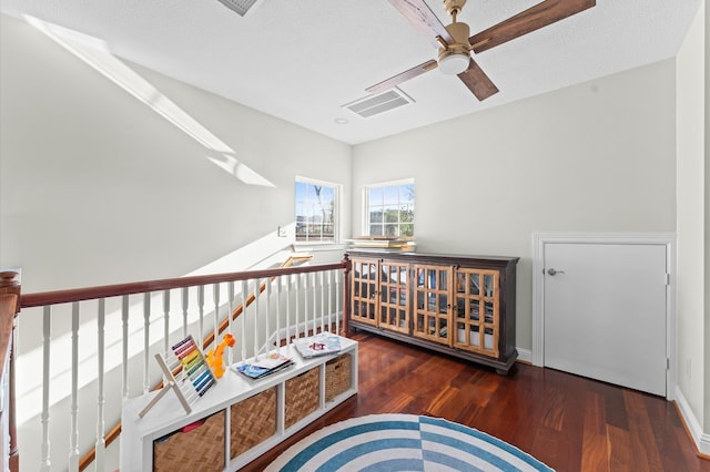 sitting room with a textured ceiling, an upstairs landing, visible vents, wood finished floors, and a ceiling fan