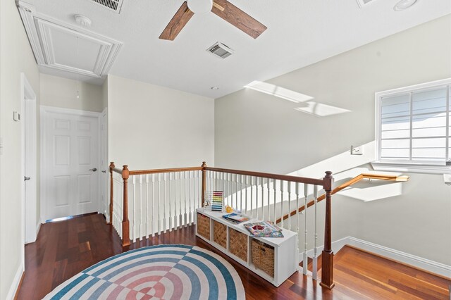 interior space with a ceiling fan, attic access, wood finished floors, baseboards, and visible vents
