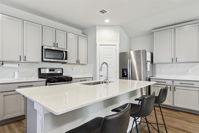 kitchen featuring a kitchen breakfast bar, stainless steel appliances, a sink, dark wood-style floors, and visible vents