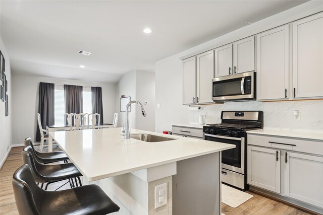 kitchen featuring decorative backsplash, stainless steel appliances, an island with sink, a sink, and light wood-style floors