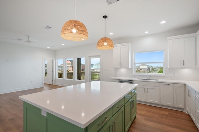 kitchen with green cabinetry, light countertops, a kitchen island, a sink, and white cabinetry