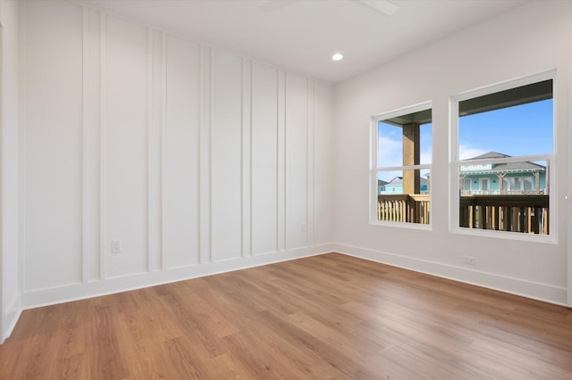 spare room featuring baseboards, a decorative wall, and light wood-type flooring