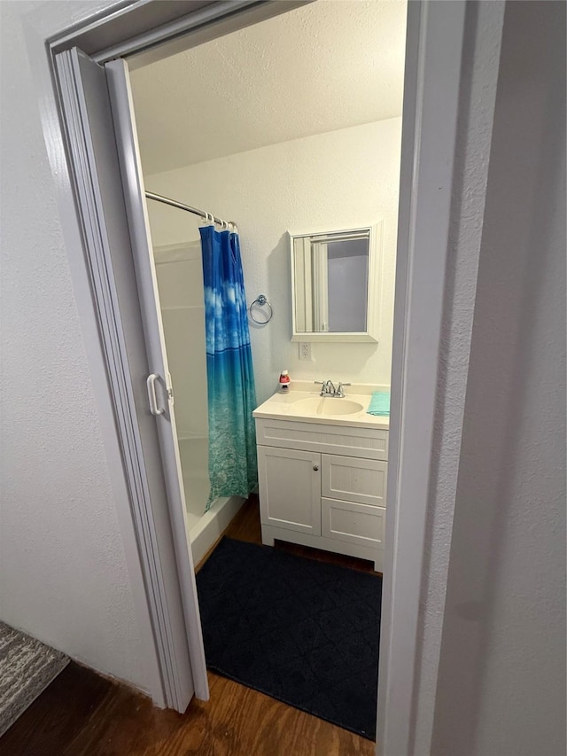 bathroom featuring vanity, a textured wall, a shower stall, and wood finished floors