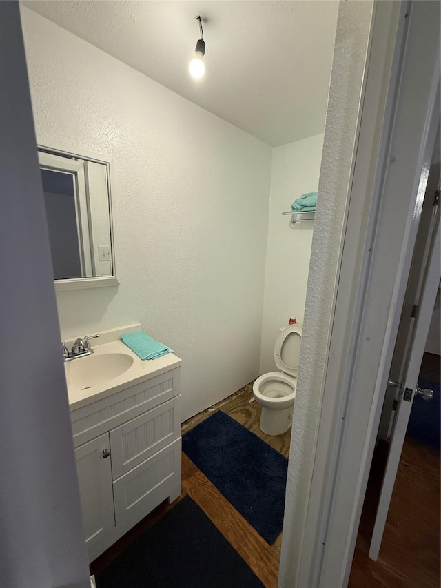 half bath featuring toilet, wood finished floors, and vanity